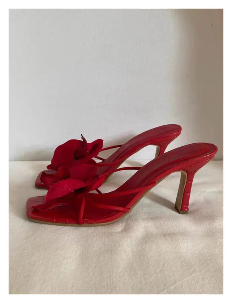 Bold red high heels embellished with a delicate white flower, ideal for adding a touch of elegance to any outfit.